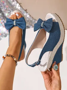 Detailaufnahme der Jeansblauen Keilsandalen mit großer Schleife und Strohabsatz.