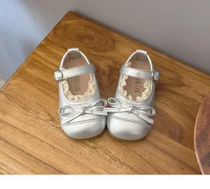 Top view of silver toddler girl Mary Janes featuring lace trim and a bow detail on wood