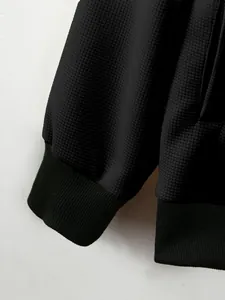 Close-up of black men's waffle knit jacket showing fabric texture and ribbed cuffs
