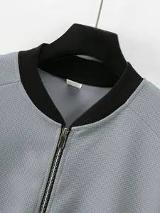 Close-up detail of a grey waffle-knit jacket featuring a black ribbed collar and silver zipper