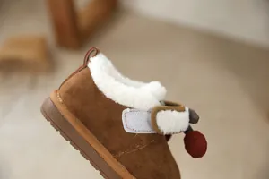 Close-up detail of brown girls' winter snow boot with soft white fur and cherry charm