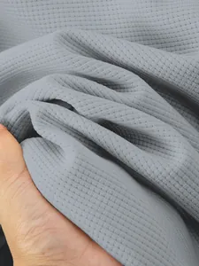 Close-up macro view of thick light grey waffle texture fabric for men's winter jacket.