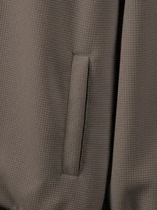 Macro view showing the textured waffle knit fabric and pocket detail of the brown jacket