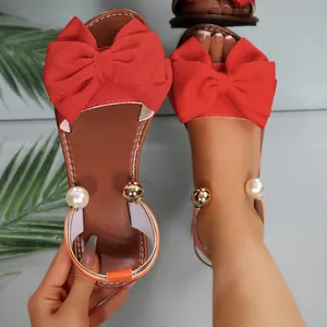 Détail de sandales plates rouges avec un grand nœud en tissu et des perles à la cheville.