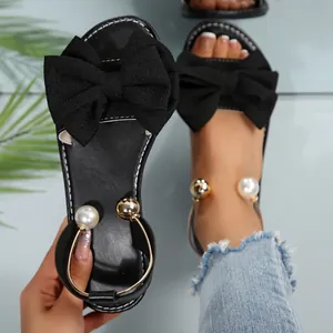 Détail de sandales plates noires avec un nœud géant et des accents de perles