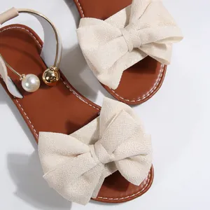 Détail du nœud en tissu beige et de la bride perlée sur des sandales plates brunes