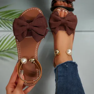 Vue détaillée de sandales plates marron avec un grand nœud en tissu et des accents de perles.