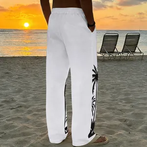 White men's beach trousers with black palm tree print shown in a sunset beach setting