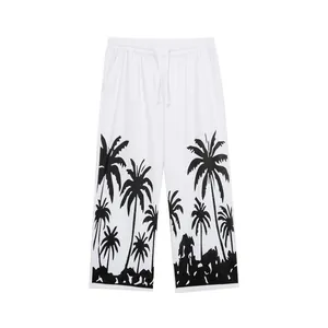 Detailed view of white men's beach pants featuring a black palm tree print at the hem.