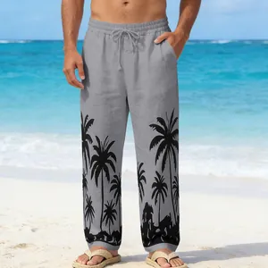 Close-up of men's grey beach pants with black palm tree prints on a beach background.