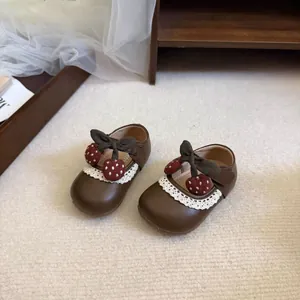 Close-up detail view of brown toddler princess shoes featuring lace trim and a strawberry bow.