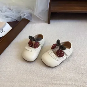 Detail view of toddler girl's cream Mary Jane shoes with lace and cherry bow decoration.