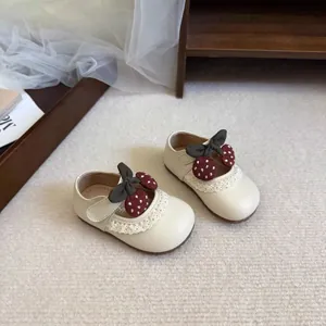 Detailed view of cream toddler shoes with lace trim and strawberry bow decoration