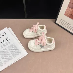 Detailed close-up of white children's sneakers featuring pink laces and a glitter star