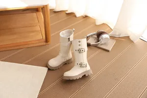 Detail der beigen Mädchen-Halbstiefel mit Vintage-Schnallen und dicker Sohle auf Holzboden.