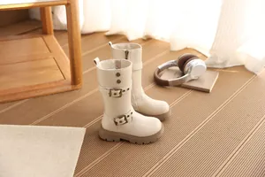Elegante cremefarbene Kinderstiefel mit doppelten Gürtelschnallen in gemütlicher Kulisse