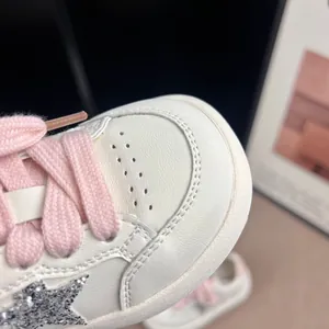 Detailed close-up of children's white sneakers with a silver glitter star and pink laces