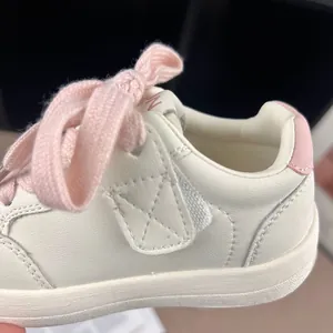 Close-up detail of white children's leather sneakers featuring pink laces and fine stitching