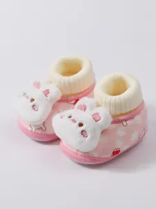 Detail view of pink plush baby booties with a cute white rabbit decoration for winter