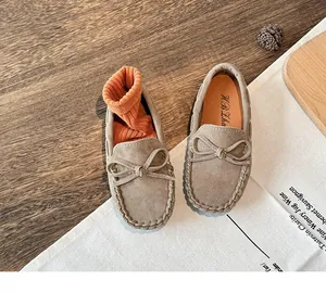 Detailed top-down view of children's khaki suede bow loafers on a rustic wooden surface