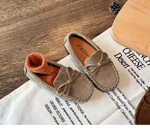 Detailed view of beige suede children's loafers with a decorative bow and stitching.