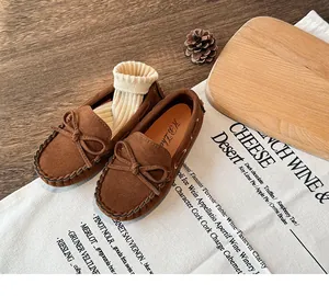 Detailed view of brown suede children's loafers with bow accent and decorative props