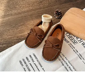 Close-up of children's brown suede loafers with bow detail on rustic wooden background