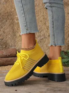 Detail view of yellow knit sneakers with thick black platform soles and lace-up design