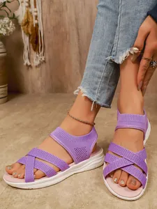 Dettaglio ravvicinato di sandali piatti in rete viola traspirante su piedi con jeans blu