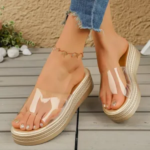 Detailed view of gold platform wedge sandals with transparent PVC strap on wooden deck