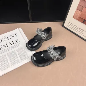 Detail of black patent leather Mary Jane shoes with grey ruffled pearl straps on a magazine.