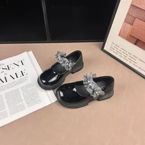 Elegant black patent leather girls' shoes with grey ruffled pearl straps on a desk.