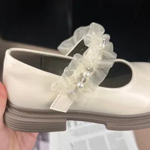 Detailed close-up of girls' cream patent leather Mary Jane shoes with pearl ruffle