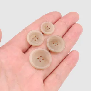 Four assorted sizes of beige four-hole resin buttons shown on a hand for scale.