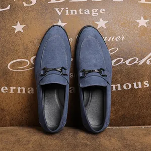 Bovenaanzicht van blauwe suède herenloafers met metalen gesp op een vintage lederen achtergrond.