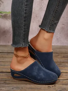Detail of women's blue wedge fur-lined clogs with white stitching on wood floor.