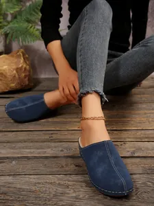 Detail view of blue suede-like closed-toe mules with white stitching on a model