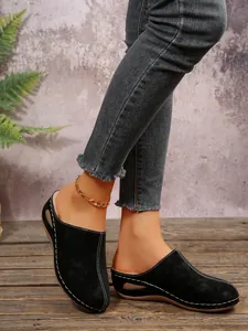Close-up of black wedge cotton slippers with white stitching and plush lining on model