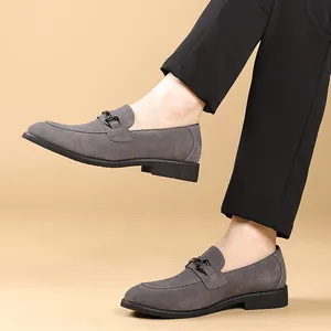 Detail van grijze suède loafers met metalen gesp gedragen door model in zwarte broek