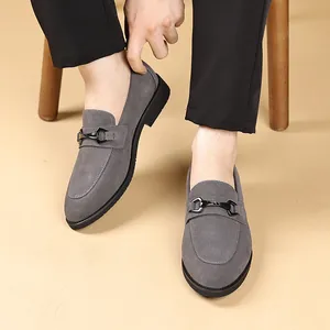 Detailopname van stijlvolle grijze suède herenloafers met een zwarte metalen gespversiering.