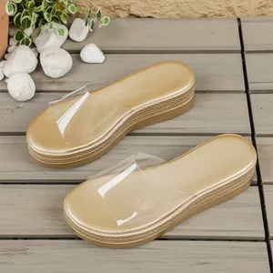 Detail view of gold platform slide sandals featuring a clear PVC strap on wooden floor