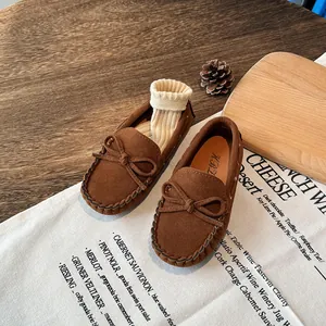 Classic brown suede children's loafers with bow detail and socks on a wooden table