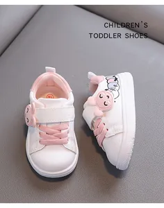 Close-up detail of white toddler shoes with pink accents and a cute pig cartoon ornament
