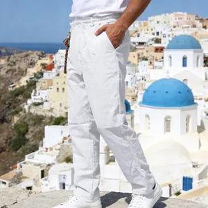 Full side view of men's white loose linen pants with drawstring in a coastal town