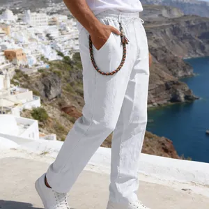 Detail view of men's loose white linen pants with woven cord accessory in coastal setting.