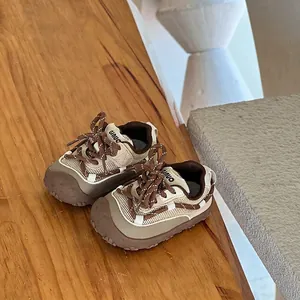 Detailed close-up view of cream and brown toddler sneakers with mesh upper on a wooden surface