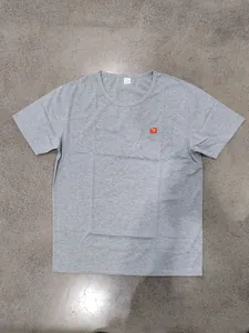 Detail of a gray oversized men's t-shirt featuring a chest pocket with an orange logo label.