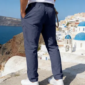 Detail of men's loose linen straight trousers in navy blue against a coastal backdrop.