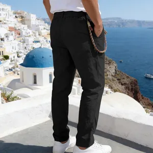Detail view of men's black loose linen casual trousers with a Mediterranean backdrop