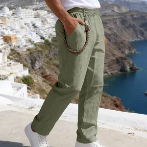 Detailed view of man wearing sage green loose linen trousers in a coastal setting